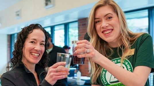 Two Binghamton dietitians smiling and holding up drinks at a campus event.