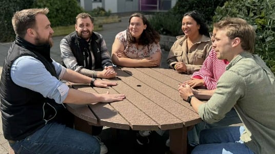 Group of interns gathered closely around a table, engaged in a lively discussion.  