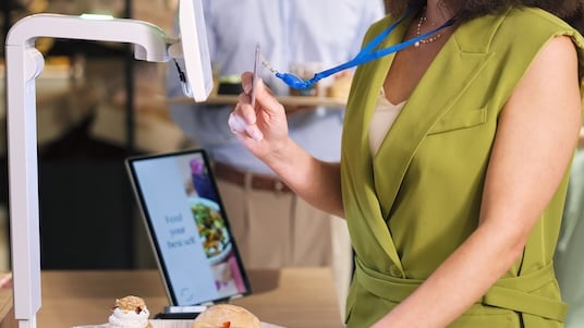 Person using a self-service food scanner to register a meal in a cafeteria setting.