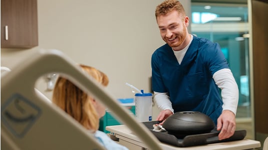 Healthcare worker offers a meal tray to a patient in a hospital bed during bedside care.