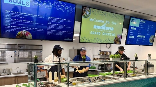 Mediterra station at SUNY New Paltz dining hall, with staff preparing meals behind the counter and digital menu boards displayed overhead.