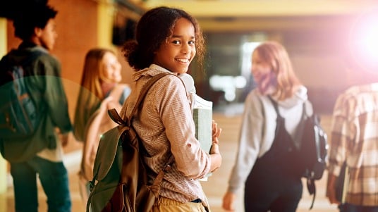 Middle school students walking down a school hallway, with one student smiling at the camera.