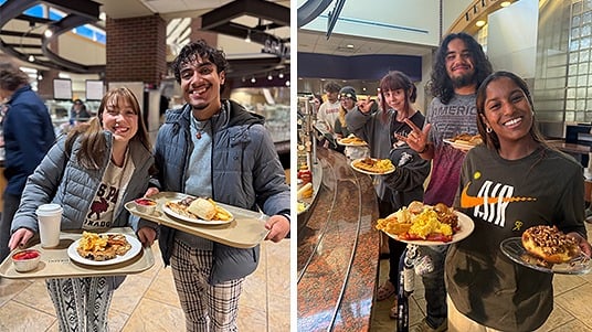Students at the University of Northern Colorado smiling while holding trays of food in a campus dining hall. 