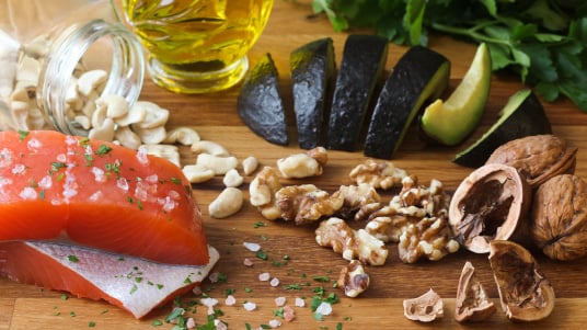 Salmon, nuts, avocado slices, and olive oil arranged on a wooden surface.