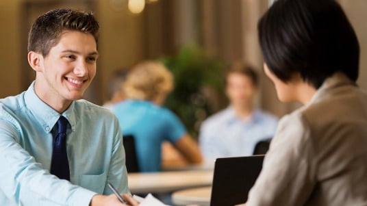 College student dressed professionally hands his resume to an interviewer at a career fair. 