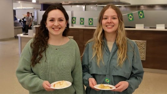 Two students smiling while holding a Brazilian dish during a Global Chef lunch at SUNY Oneonta. 
