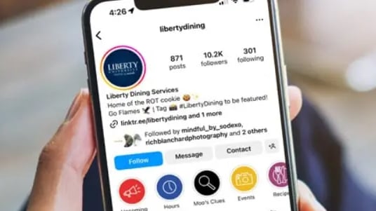 Hand holding smartphone displaying Liberty Dining social media profile with follower and engagement details.