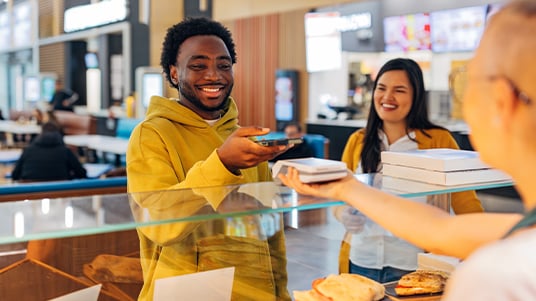Customer makes a contactless payment and receives takeout containers at a food counter.