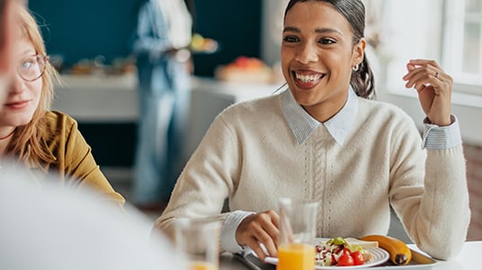 Person enjoying a meal with salad and juice while seated at a dining table with others.