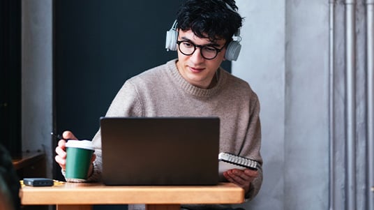 Group of people sitting outdoors near colorful structures, sharing slices of pizza and chatting together in a casual urban setting with food trucks in the background.