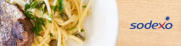 Close-up of a plate of pasta garnished with capers and parsley, served alongside a piece of cooked meat.