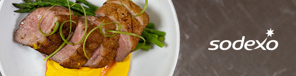 Sliced duck breast with asparagus and yellow sauce on a white plate, with Sodexo logo on the right.