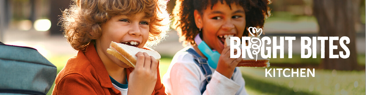 Two children eating sandwiches outdoors, with Bright Bites Kitchen logo on the right