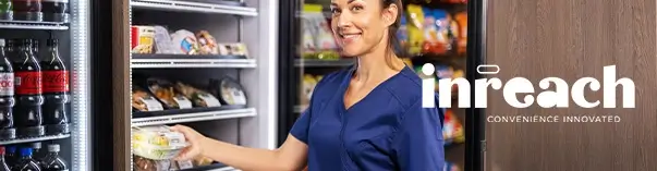 Person in a blue uniform reaches into a refrigerated display case with sandwiches and drinks; shelves with snacks in the background.