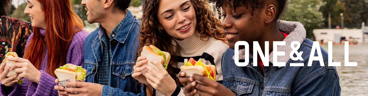 Group of people sharing sandwiches outdoors, with the words ONE & ALL displayed on the right