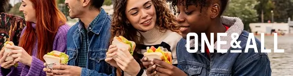 Group of people sitting outdoors, each holding and eating sandwiches.