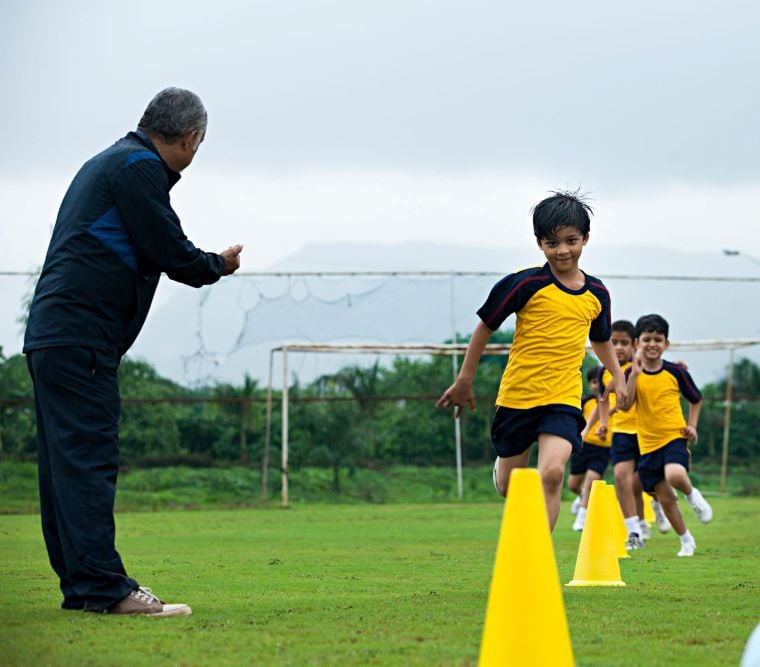 A man instructs children on running efficiently through cones