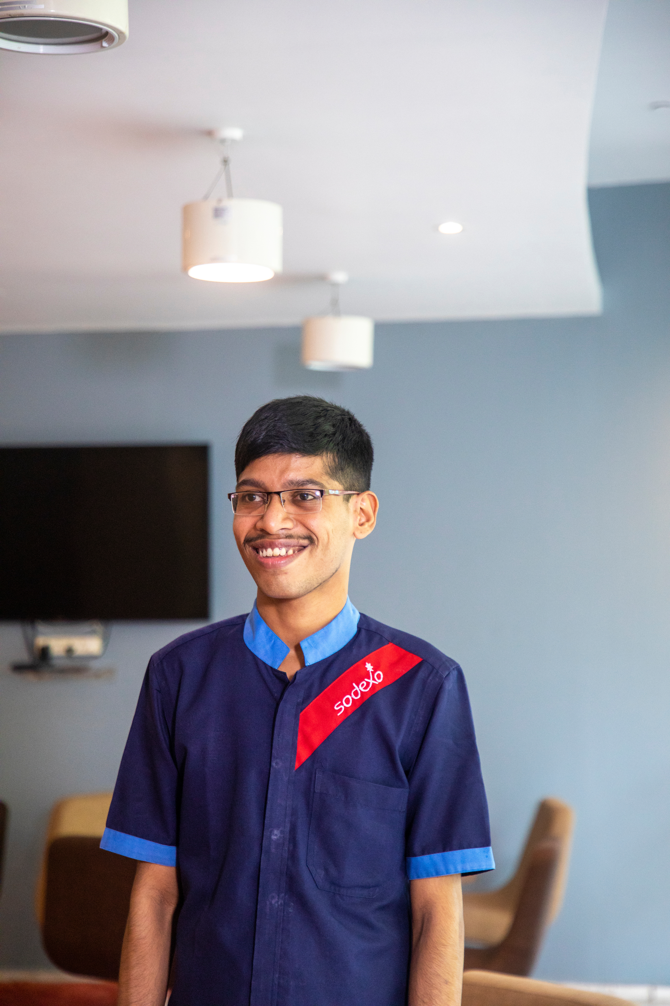 A Sodexo employee wearing glasses and a blue shirt, smiling.