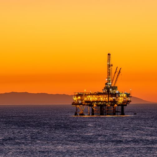 An oil rig at sunset, with colorful skies and calm waters.