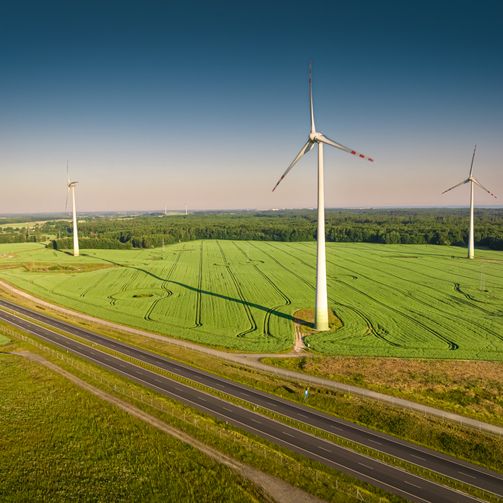 A wind farm by a highway in lush countryside.