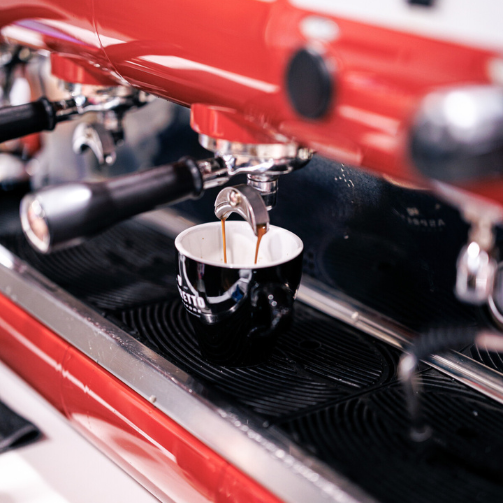Espresso shot being filetered into a black mug while resting on a red coffee machine