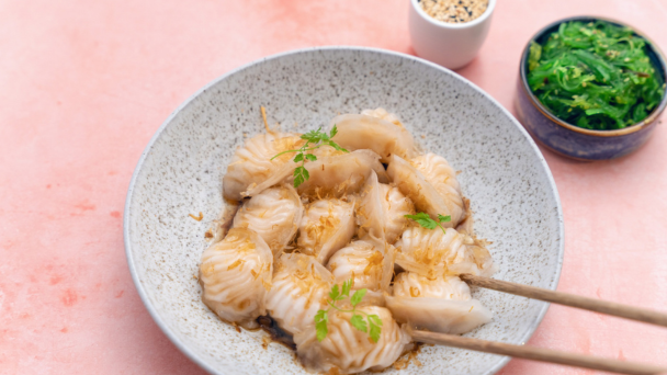 A plate of dumplings being picked up by chopsticks and a wakame salad.