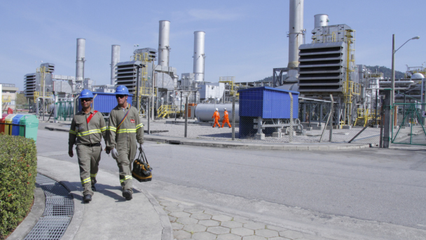 Two men in hard hats walking in front of an energy plant