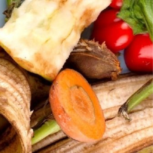 A pile of discarded fruits and vegetables including an apple core, carrot top, banana peel, plum seed and bell pepper.