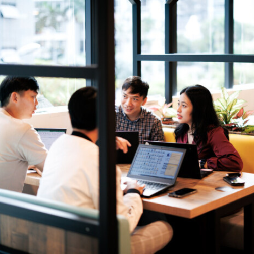 Four university students sitting in a booth with their laptops talking.