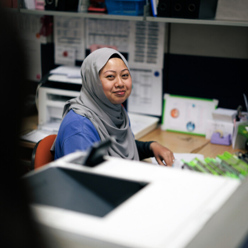 a woman with a hijab is smiling while doing office work