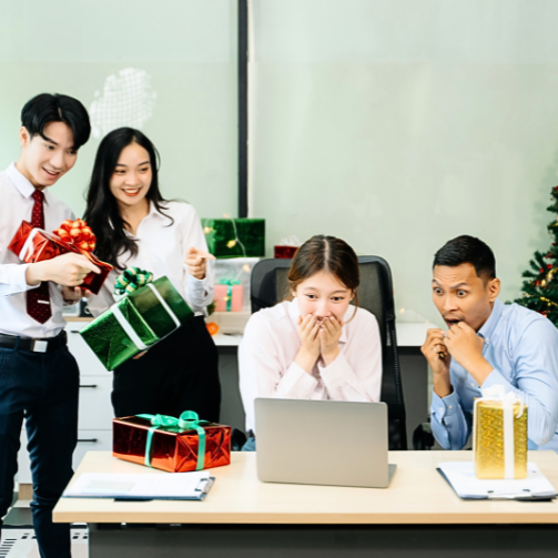 Four colleagues sitting around a computer with Christmas gifts.