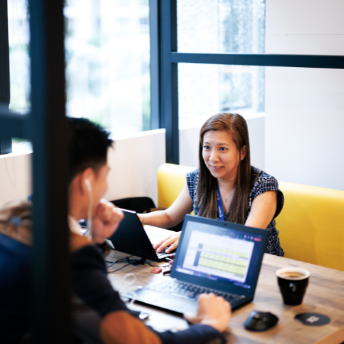 a woman in a booth talking to a man on his computer