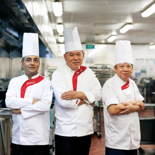 three male chefs are standing with crossed arms in a kitchen