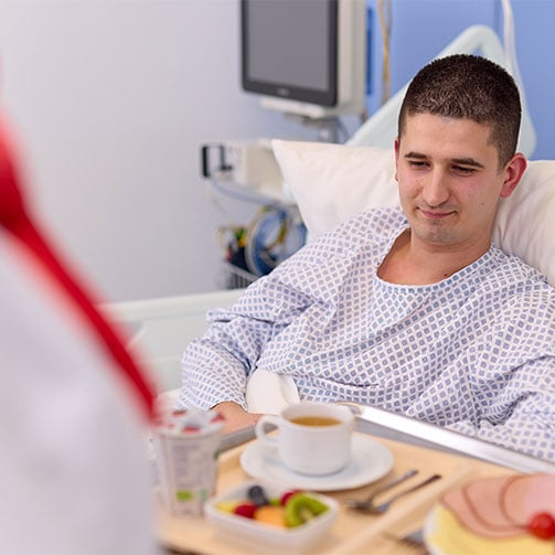 Junger Patient im Krankenhausbett bekommt ein gesundes Fruehstueck serviert.