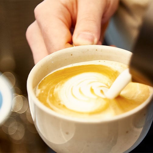 Ein Barista bereitet einen Cappuccino mit Milchschaum zu.