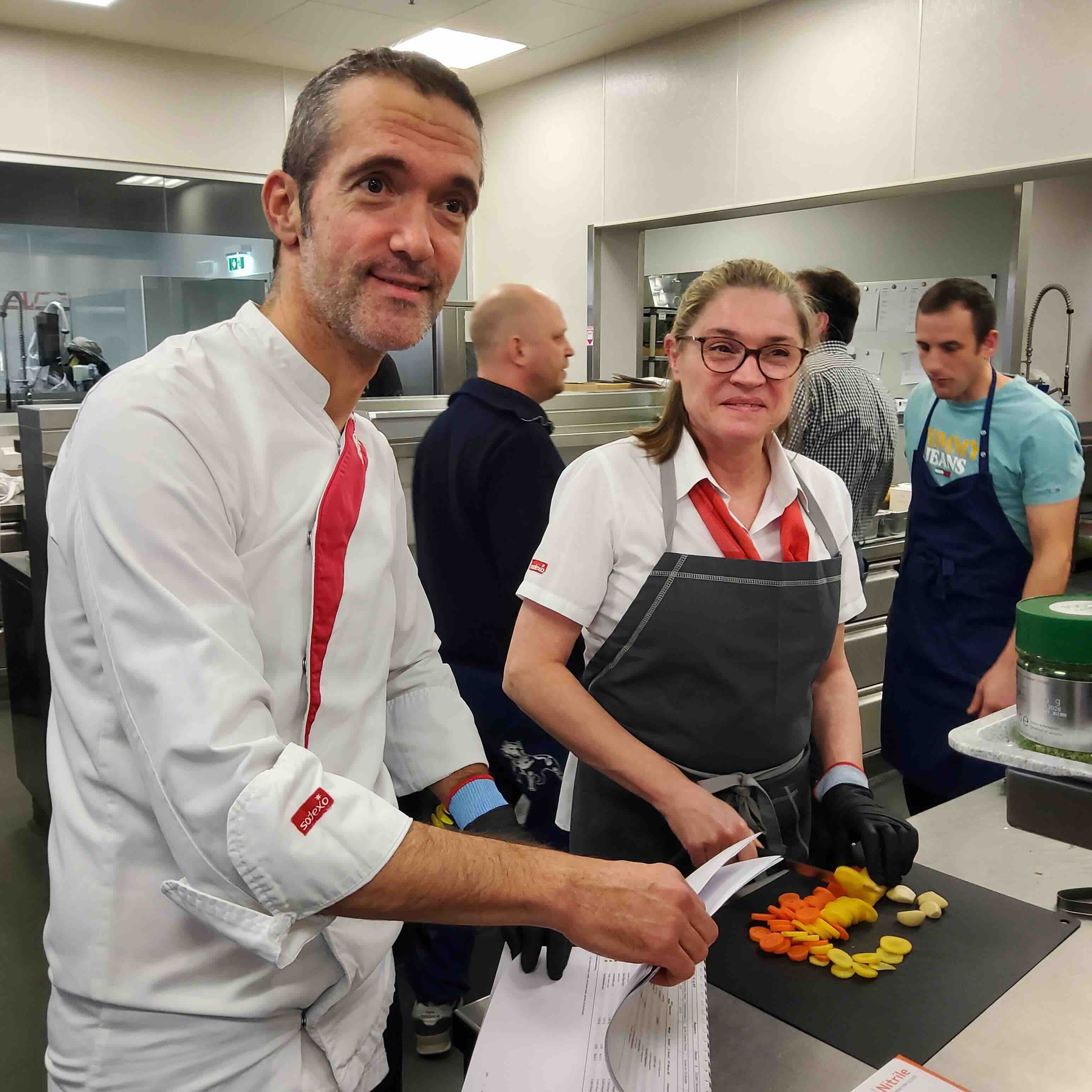 Kompetentes Kuechenpersonal bespricht ein Rezept und schneidet Gemuese.