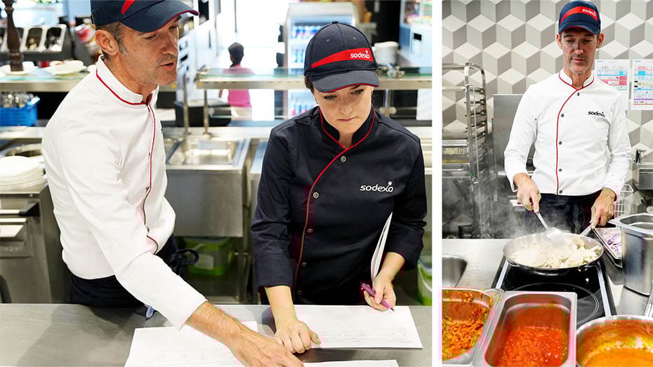Personal von Sodexo unterhaelt sich in Kueche ueber den Speiseplan. Koch braet Fleisch in einem Wok mit verschiedenen Saucen an.