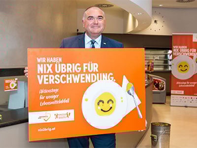 Herr Michael Freitag haelt großes, oranges Plakat gegen Verschwendung