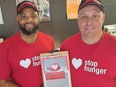 Zwei Maenner in roten Stop Hunger Shirts halten Tafel