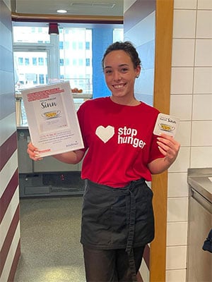 Laechelnde Frau mit Stop Hunger Shirt die Buch und Untersetzer stolz praesentiert