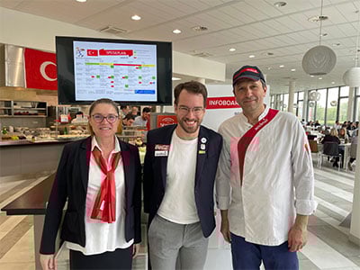 Personal in Sodexo Arbeitskleidung freut sich vor Betriebskueche ueber Besuch von Paraolympic-Schwimmer Andreas Ornea.