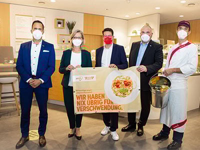 Personal vor Kueche mit Schild gegen Lebensmittelverschwendung