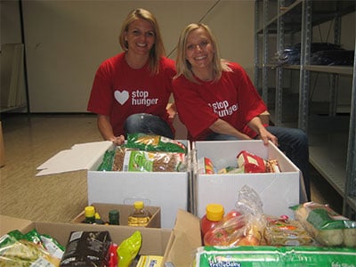 Zwei Frauen im Stop Hunger Shirt mit Kisten voller Lebensmittel