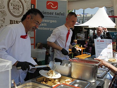 Mitarbeiter portionieren Speisen auf Teller bei Essensausgabe