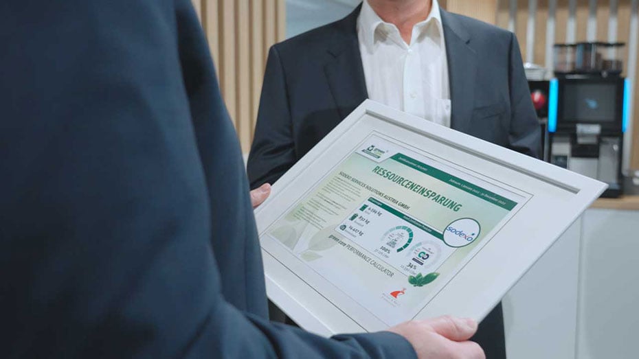 Maenner im Anzug, einer haelt Bilderrahmen zu Ressourceneinsparung