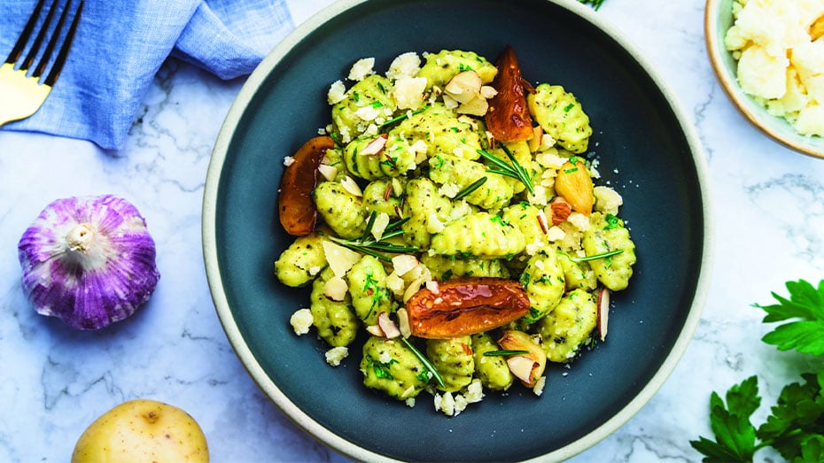 Speiseteller voller Gnocchi aus Kartoffeln, mit Pesto, Rosmarin, Petersilie, Knoblauch und Nuessen.