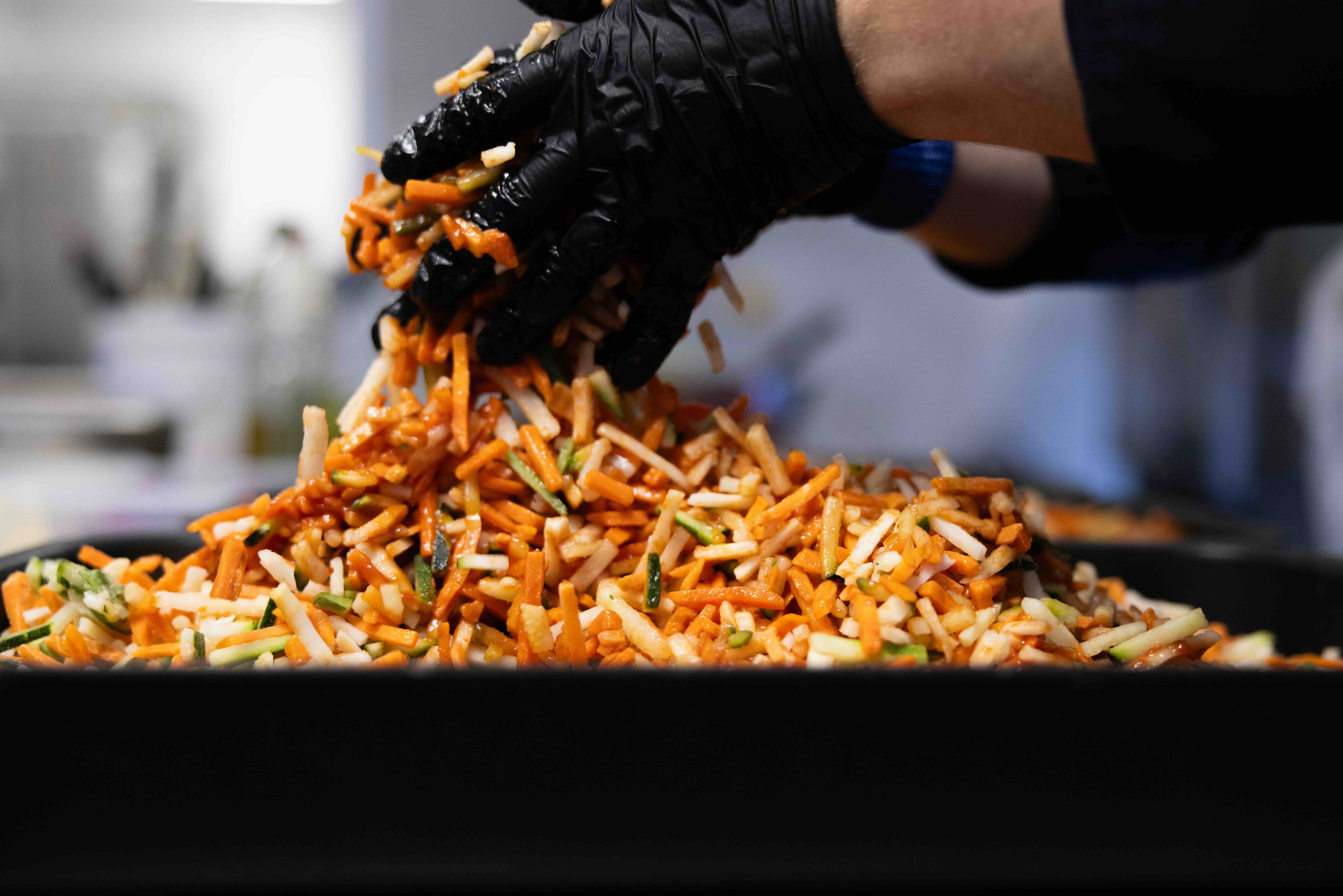Koch vermischt mit schwarzen Hygiene- Handschuhen kleine Gemuesesticks mit Sauce