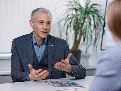 Mann in Anzug erklaert sitzend bei Schreibtisch
