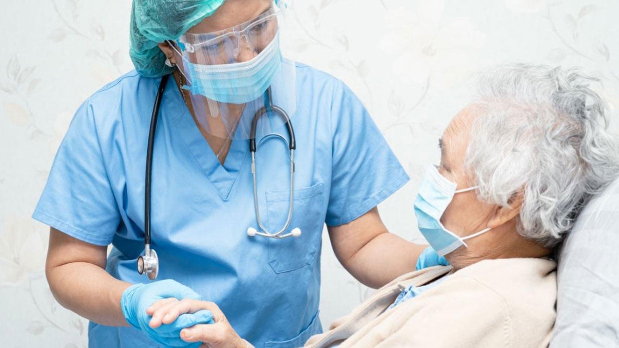 Aerztin mit Hygieneausruestung kuemmert sich um aeltere Dame