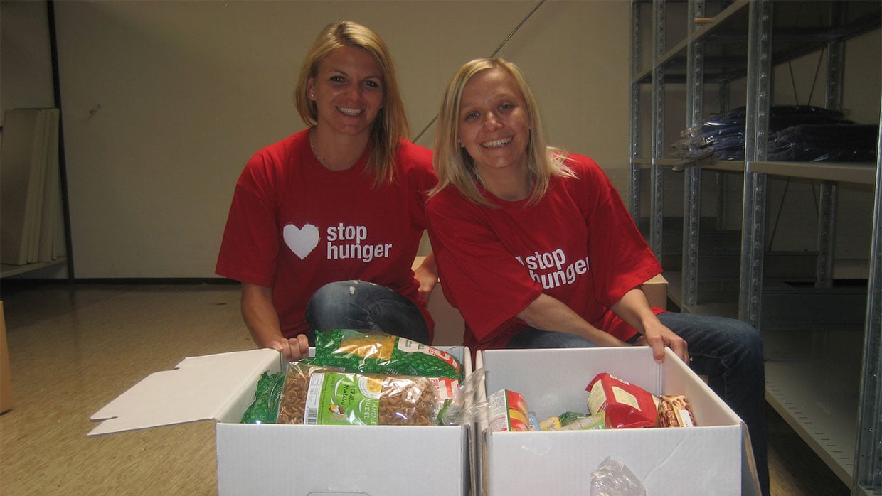 Zwei Frauen im Stop Hunger Shirt mit Kisten voller Lebensmittel